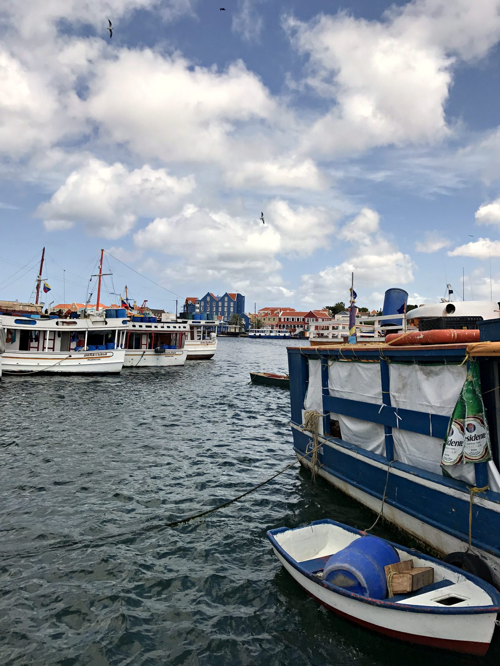 Small boats in a Willemstad harbor with colorful buildings behind