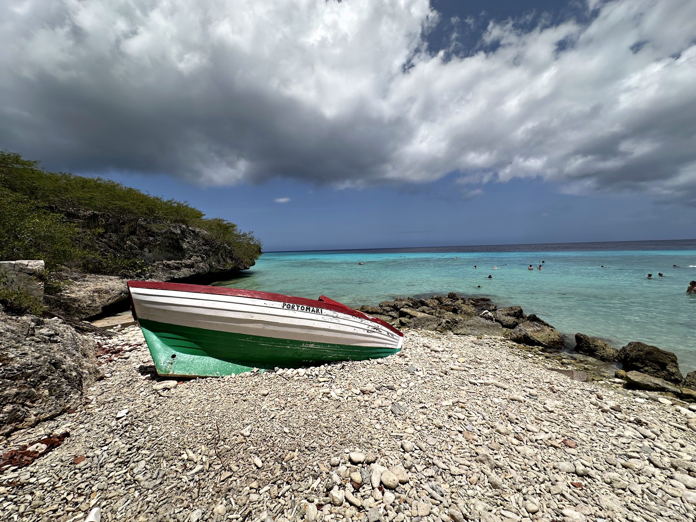 A small boat pulled up on a rocky shore beside turquoise water under dramatic clouds