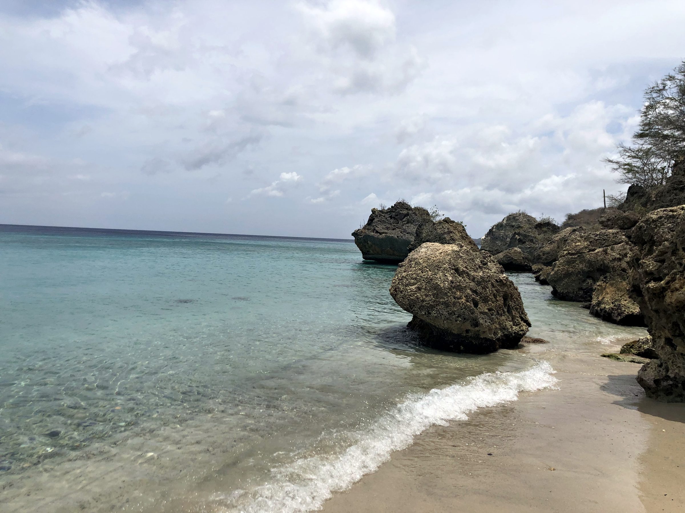 Calm turquoise water lapping a sandy beach with large rocks offshore