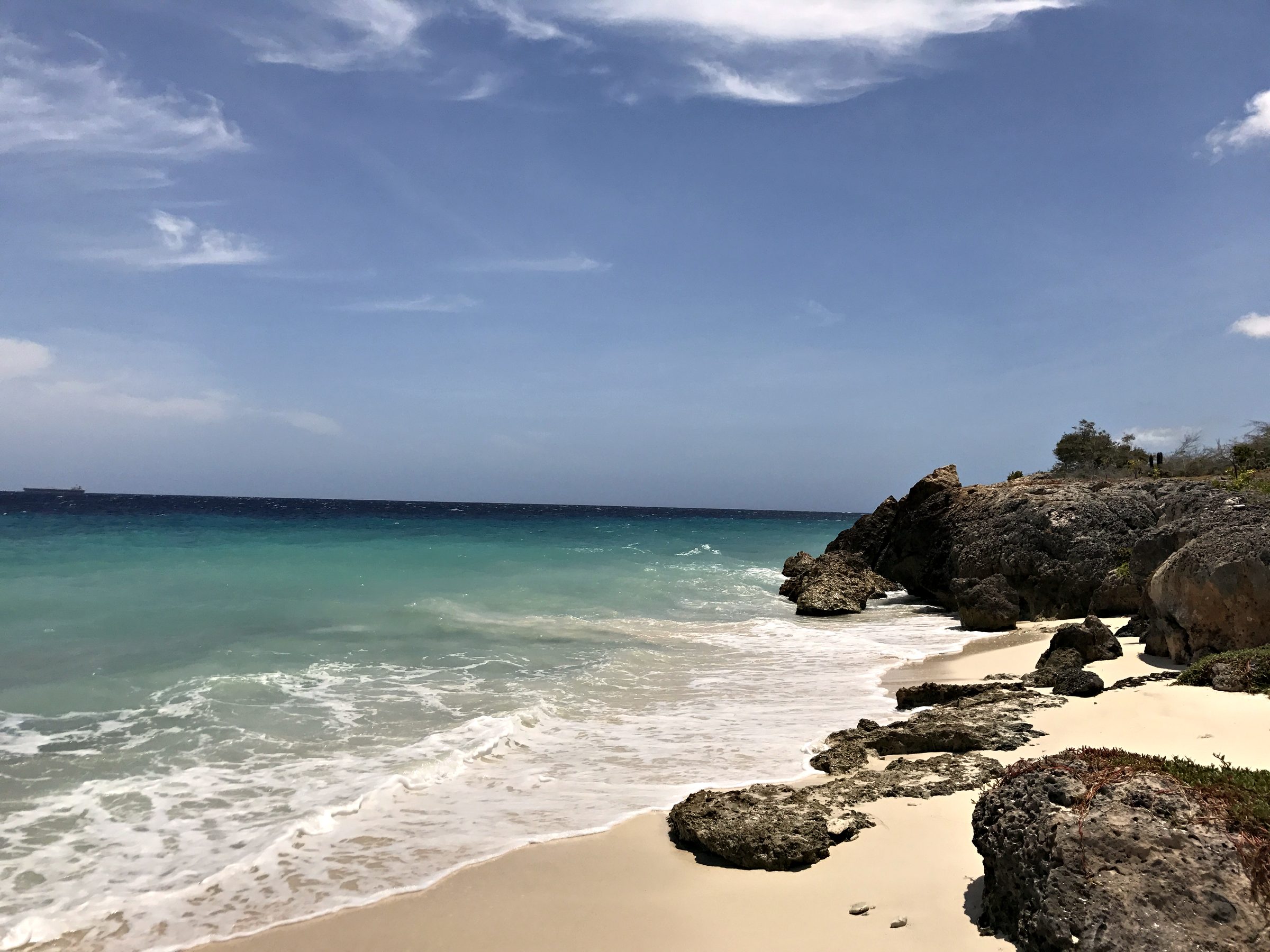 Turquoise water and white sand beside dark rocks in Curaçao