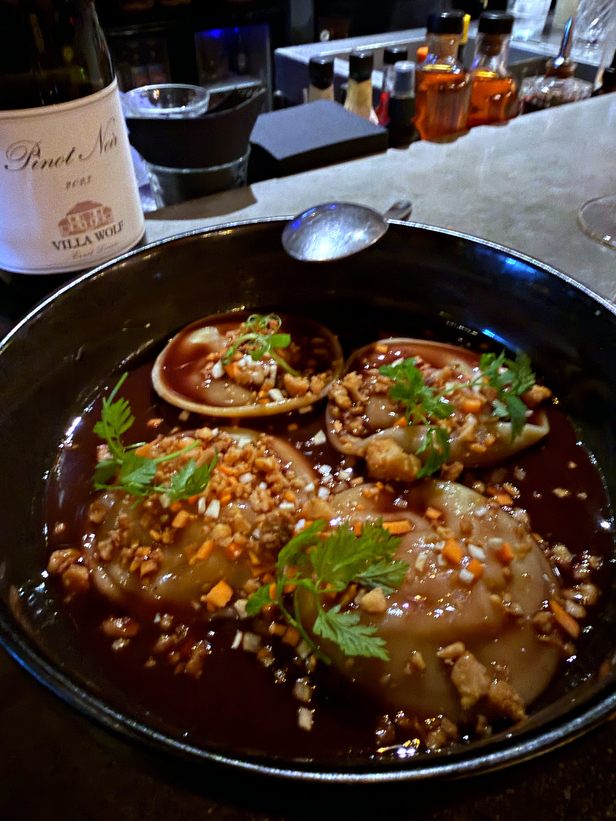 Gyoza in a dark bowl with herbs and sauce at BKLYN