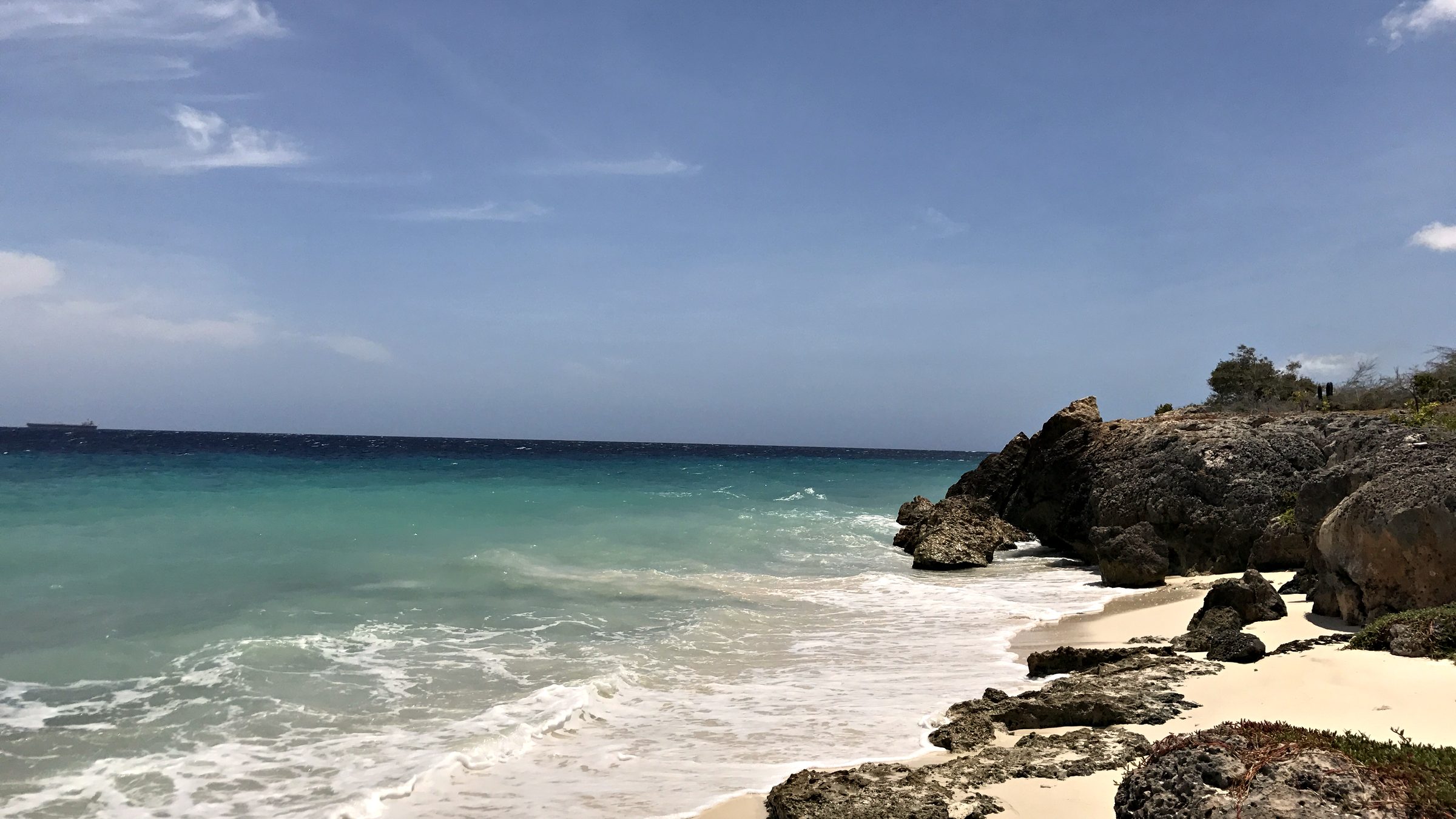 Turquoise water meeting a sandy beach and dark rocks under a blue sky in Curaçao