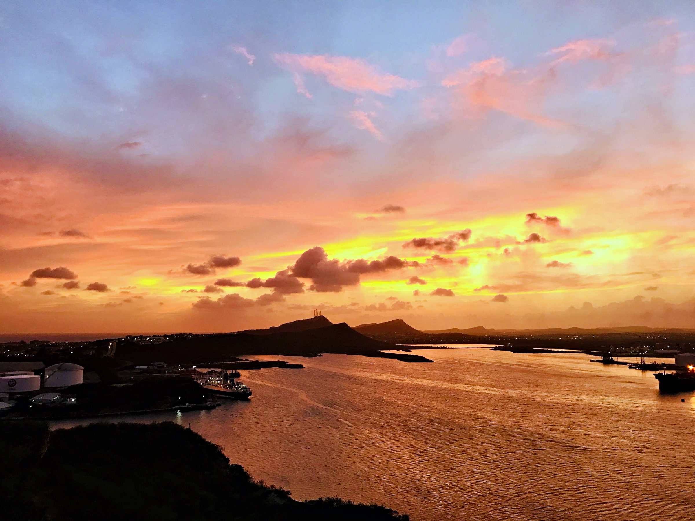 Vivid orange sunset over a calm bay with hills on the horizon