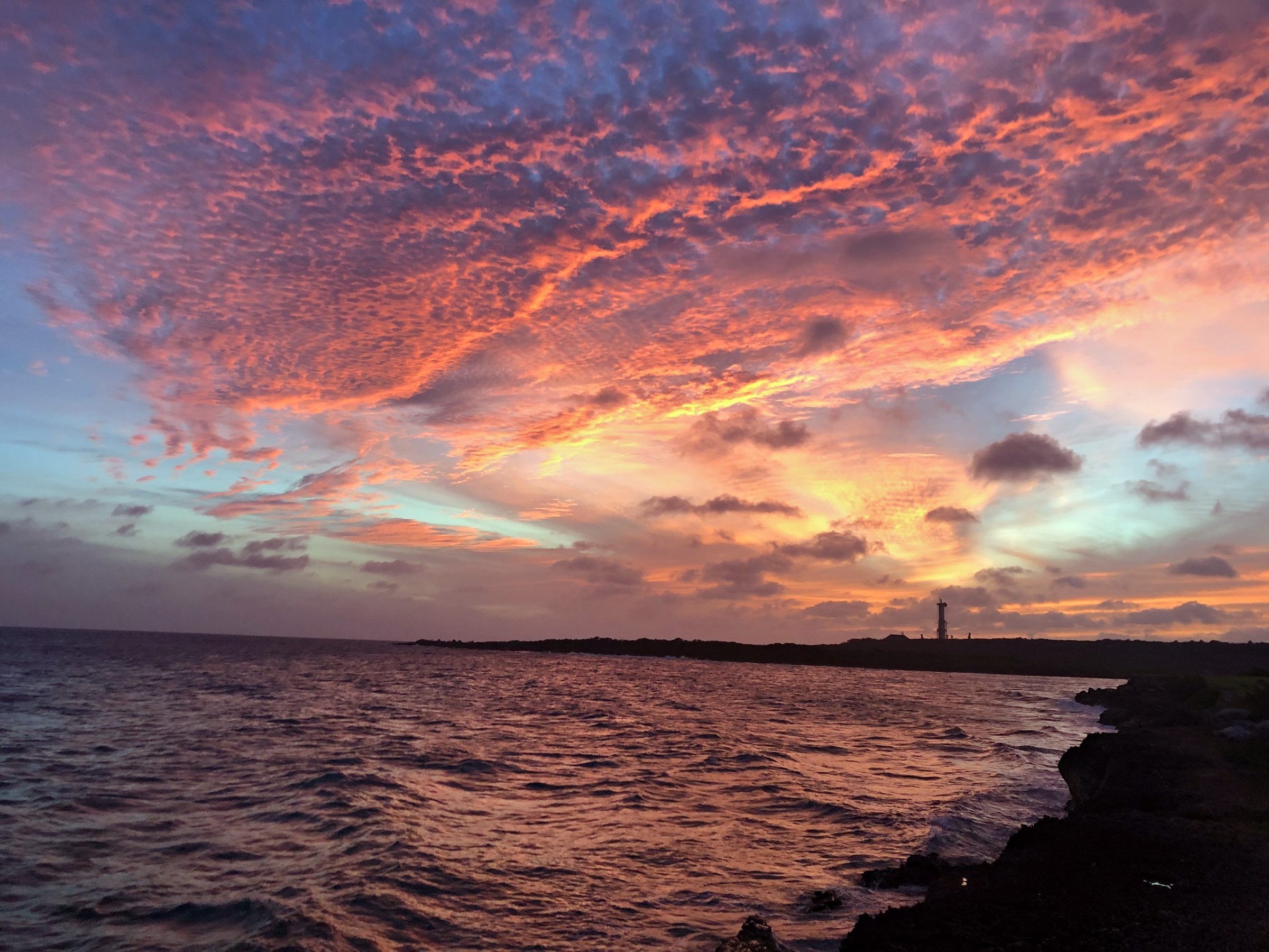Pink and red clouds at sunset over the sea and a rocky shoreline
