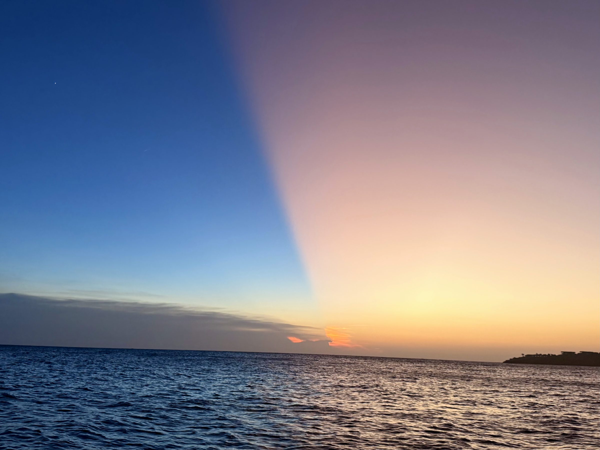 A sunset with a striking split of light and shadow across the sky over the sea