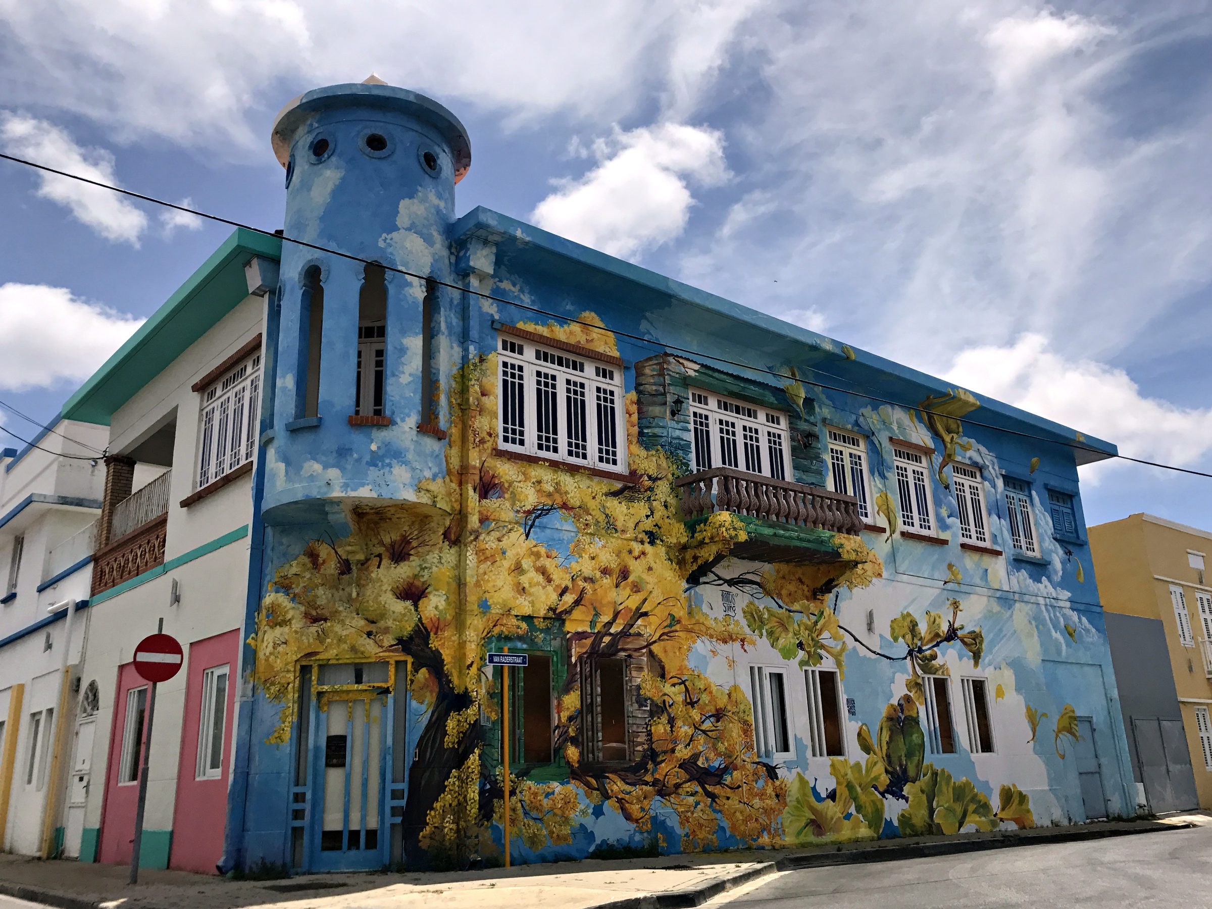 Two-story building covered in a colorful mural under a blue sky in Curaçao